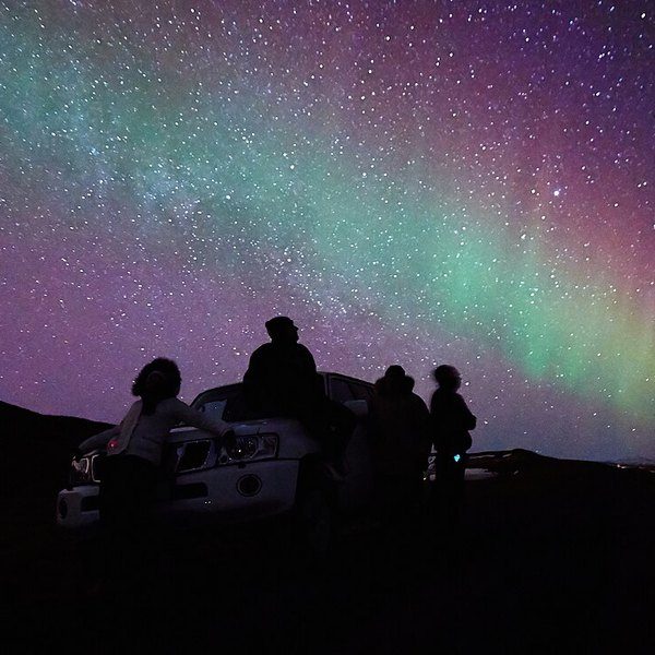 Un petit groupe de personnes en silhouette regardant une aurore boréale