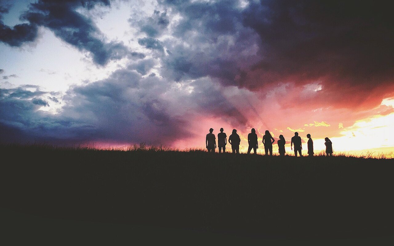 Un groupe de personnes en silhouette sous un ciel d’orage